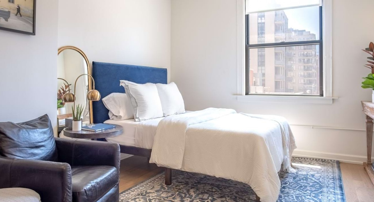 Bright bedroom at The Bush Temple in Chicago, featuring a comfortable bed, stylish decor, and a large window overlooking the city