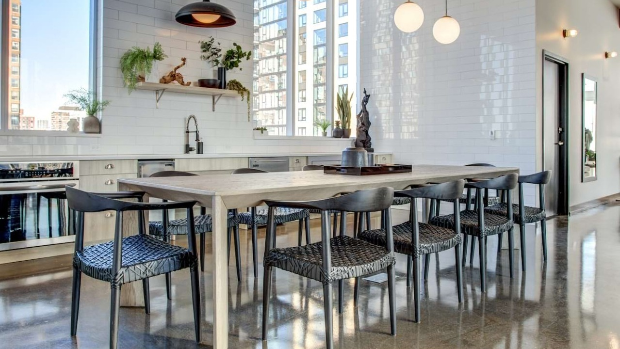 Modern chef's kitchen and dining area at The Bush Temple in Chicago, featuring a long communal table, white subway tiles, and city views
