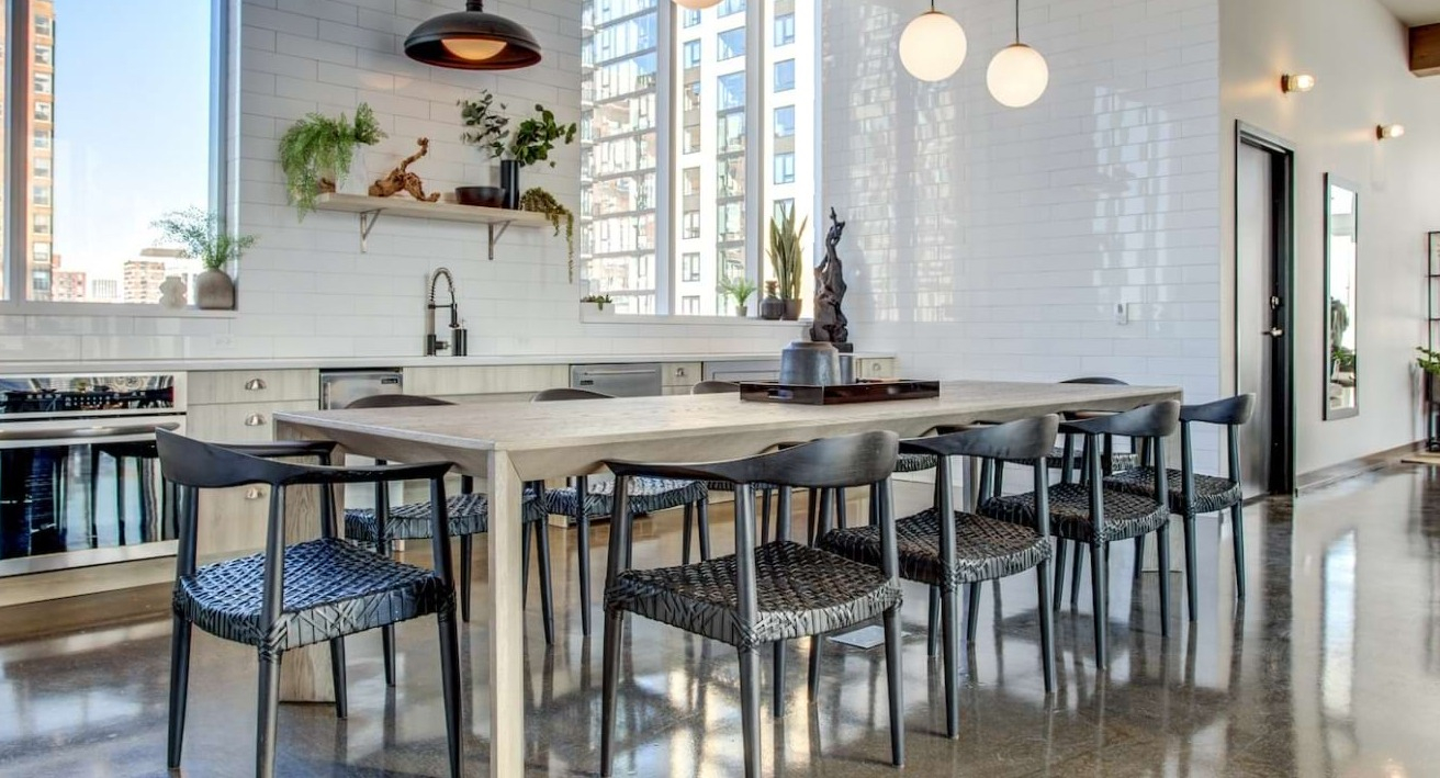Modern chef's kitchen and dining area at The Bush Temple in Chicago, featuring a long communal table, white subway tiles, and city views