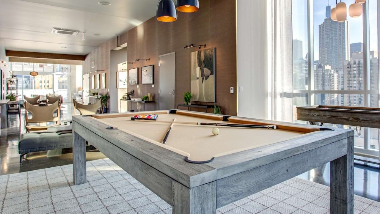 Stylish game room at The Bush Temple in Chicago, featuring a pool table, shuffleboard, and expansive city views through large windows