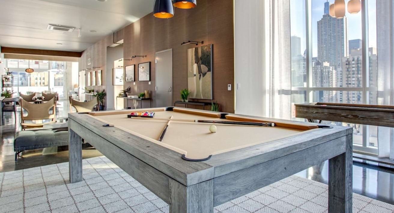 Stylish game room at The Bush Temple in Chicago, featuring a pool table, shuffleboard, and expansive city views through large windows