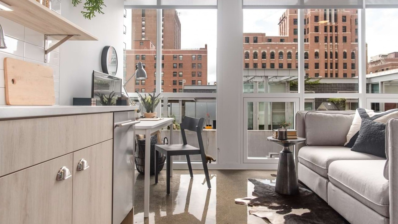 Modern studio apartment kitchen and living area at The Bush Temple in Chicago, featuring a light wood kitchen and cozy sofa