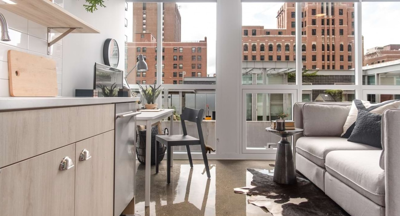Modern studio apartment kitchen and living area at The Bush Temple in Chicago, featuring a light wood kitchen and cozy sofa