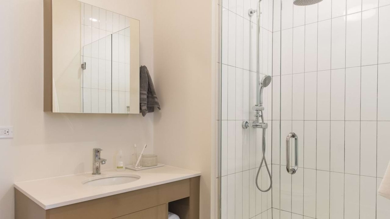 Modern apartment bathroom at The Bush Temple in Chicago, featuring a sleek vanity, mirror, and a spacious walk-in shower