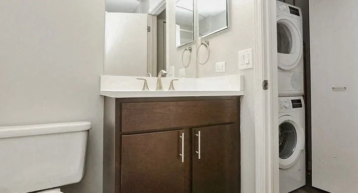 Bathroom with modern vanity, toilet, and a convenient in-unit stacked washer and dryer at Carriage House Lofts in Chicago