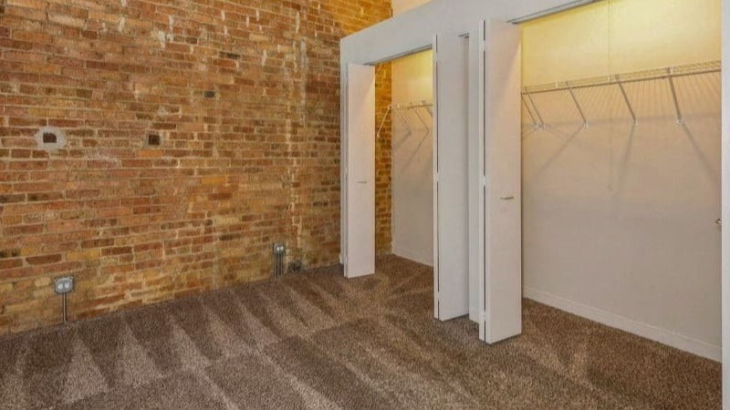 Bedroom space with an exposed brick wall and open walk-in closets, providing ample storage at Carriage House Lofts in Chicago