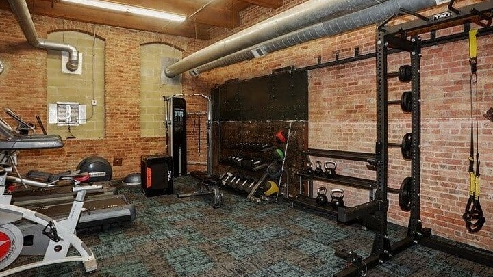 Building fitness center with various exercise equipment and exposed brick walls at Carriage House Lofts in Chicago