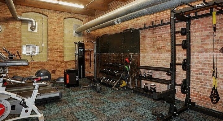 Building fitness center with various exercise equipment and exposed brick walls at Carriage House Lofts in Chicago