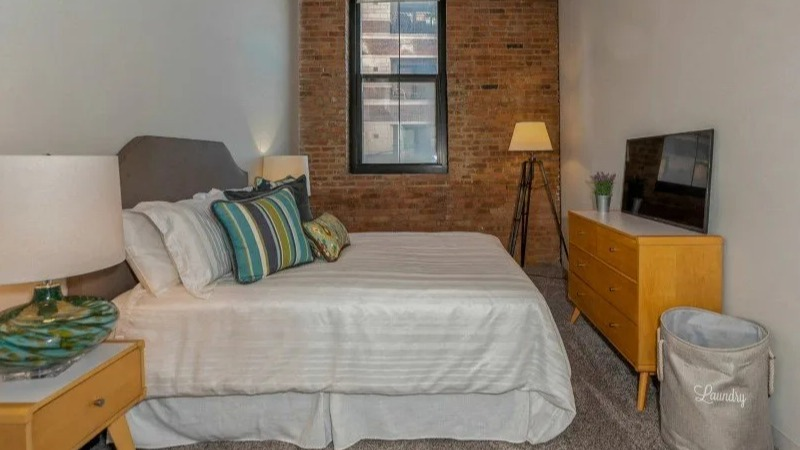 Furnished cozy bedroom with a comfortable bed, nightstands, and a dresser at Carriage House Lofts in Chicago