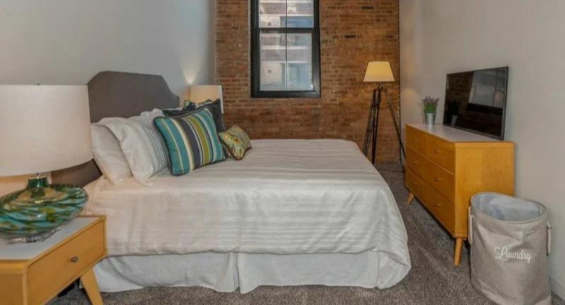 Furnished cozy bedroom with a comfortable bed, nightstands, and a dresser at Carriage House Lofts in Chicago