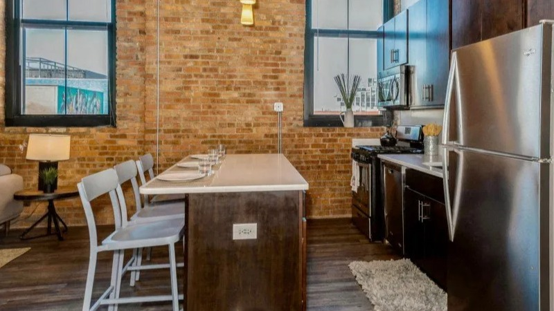 Kitchen and dining area with stainless steel appliances, modern island seating, and exposed brick walls at Carriage House Lofts in Chicago