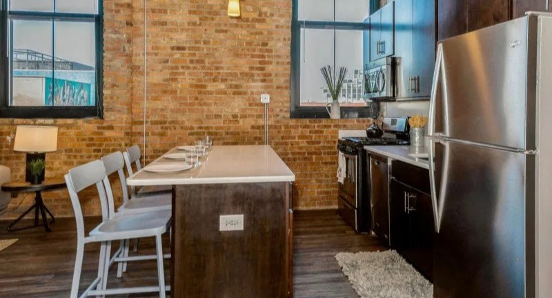 Kitchen and dining area with stainless steel appliances, modern island seating, and exposed brick walls at Carriage House Lofts in Chicago