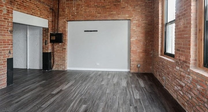 Open-concept living area with exposed brick walls, high ceilings, and hard wood floors at Carriage House Lofts in Chicago