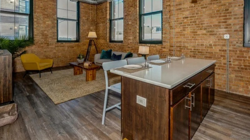 Open concept living and kitchen area with stylish furniture, exposed brick, and large windows at Carriage House Lofts in Chicago