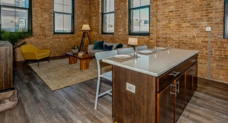 Open concept living and kitchen area with stylish furniture, exposed brick, and large windows at Carriage House Lofts in Chicago