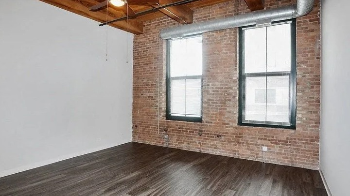 Spacious loft bedroom with exposed brick, large windows, and high ceilings at Carriage House Lofts in Chicago