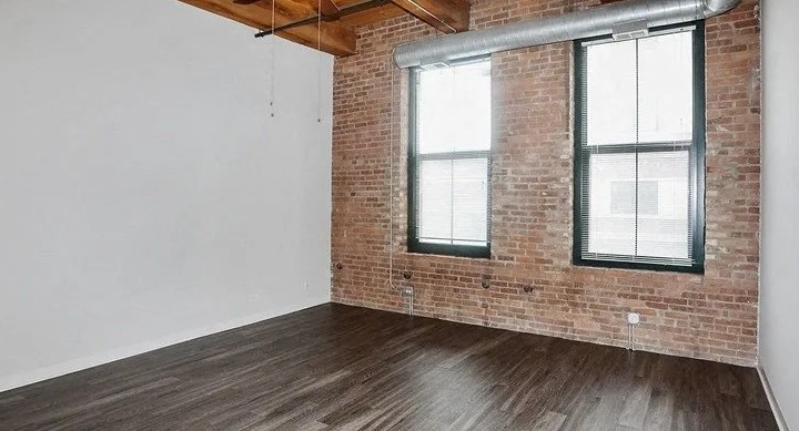 Spacious loft bedroom with exposed brick, large windows, and high ceilings at Carriage House Lofts in Chicago