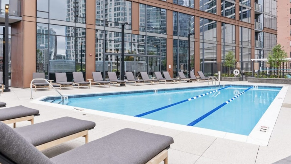 Outdoor swimming pool surrounded by modern lounge seating, set against the striking exterior of Cassidy on Canal apartments in Chicago