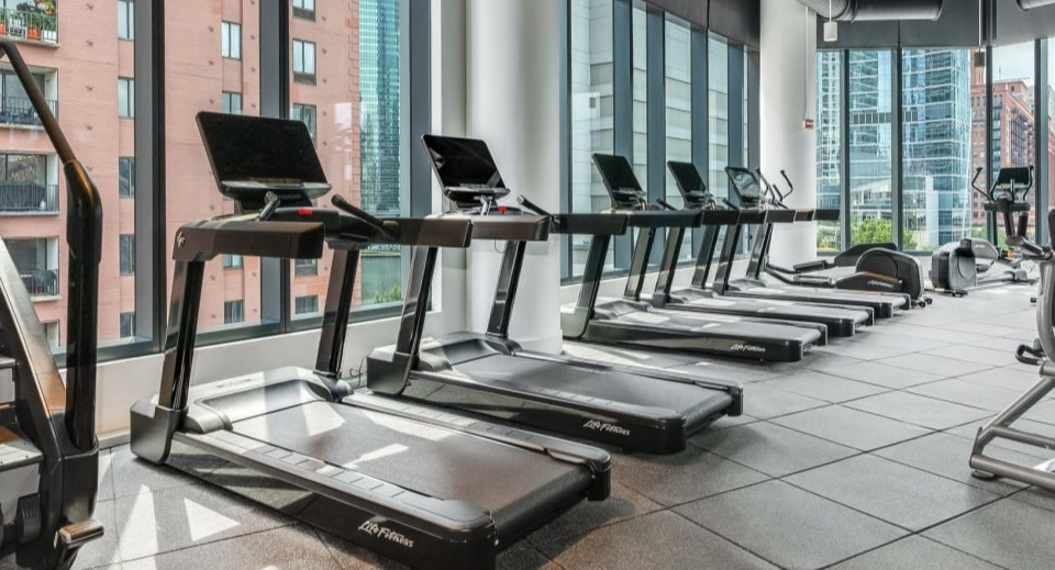 State-of-the-art fitness center with a row of treadmills and various cardio machines, offering city views at Cassidy on Canal apartments in Chicago