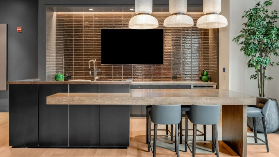 Stylish communal kitchen island with seating, a large television, and modern pendant lights at Cassidy on Canal apartments in Chicago
