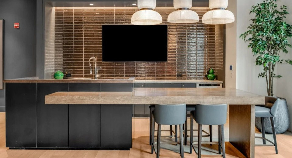 Stylish communal kitchen island with seating, a large television, and modern pendant lights at Cassidy on Canal apartments in Chicago