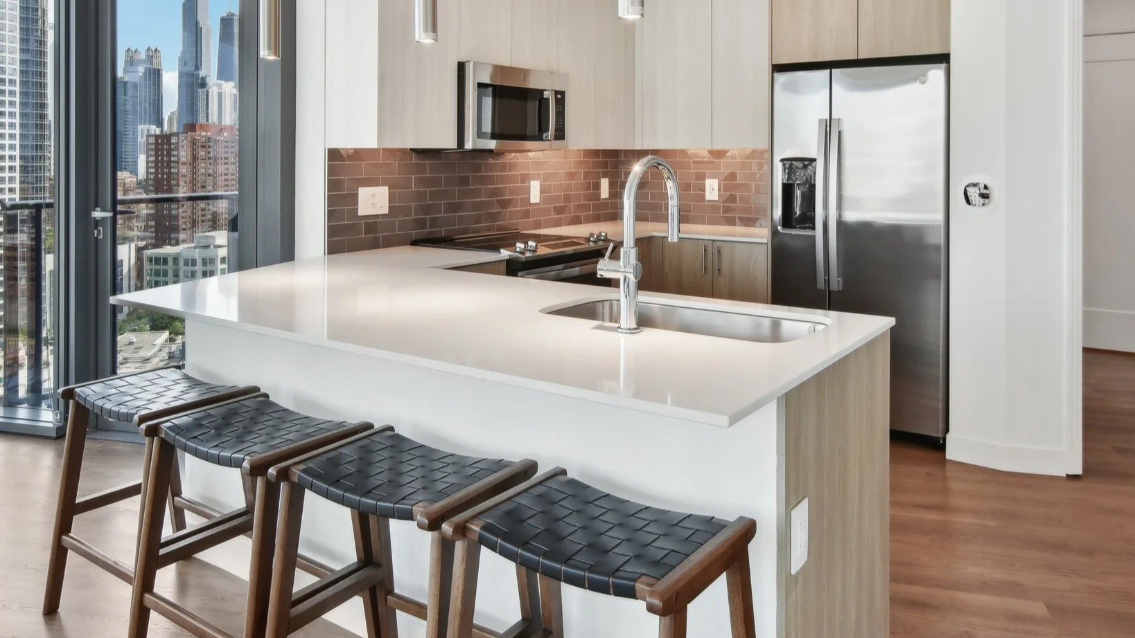 Sleek, modern apartment kitchen with a breakfast bar, stainless steel appliances, and large windows offering city views at Cassidy on Canal in Chicago