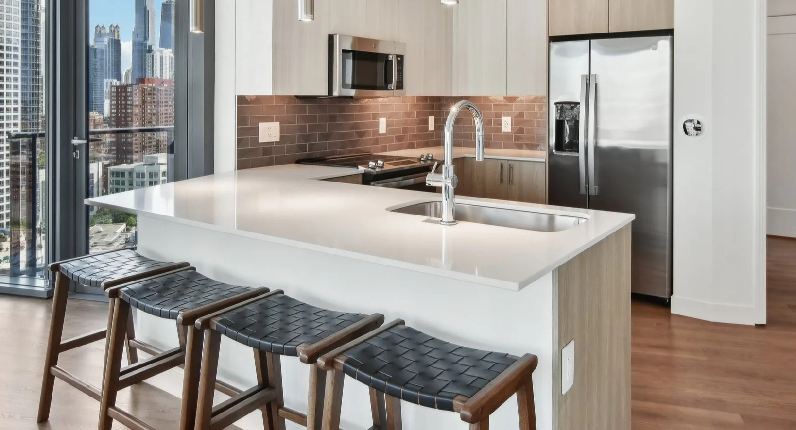 Sleek, modern apartment kitchen with a breakfast bar, stainless steel appliances, and large windows offering city views at Cassidy on Canal in Chicago