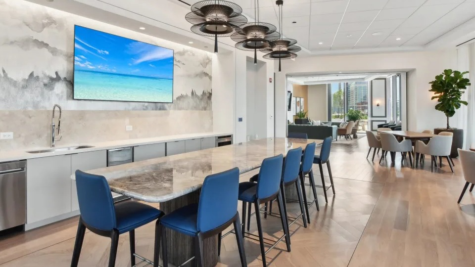 Modern resident lounge featuring a long communal kitchen island with blue bar stools and a dining area at Cassidy on Canal in Chicago