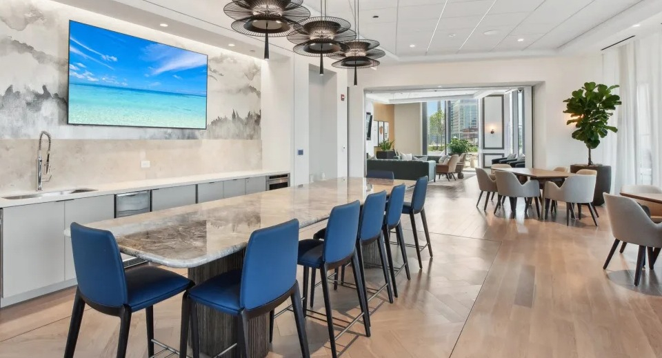 Modern resident lounge featuring a long communal kitchen island with blue bar stools and a dining area at Cassidy on Canal in Chicago