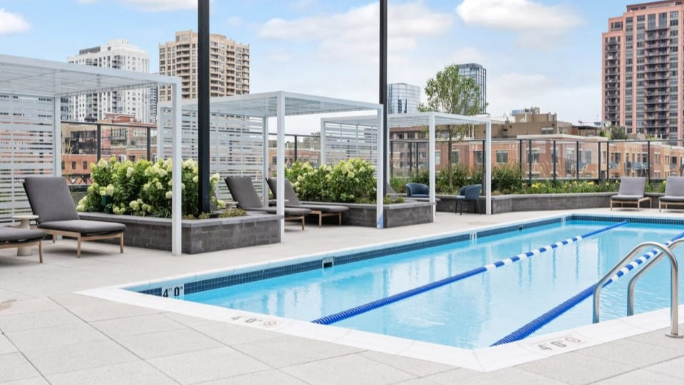 Rooftop swimming pool with lane lines and comfortable lounge chairs, offering stunning city skyline views at Cassidy on Canal apartments in Chicago