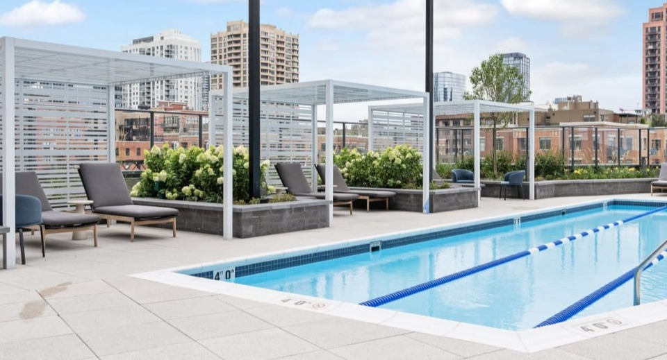 Rooftop swimming pool with lane lines and comfortable lounge chairs, offering stunning city skyline views at Cassidy on Canal apartments in Chicago