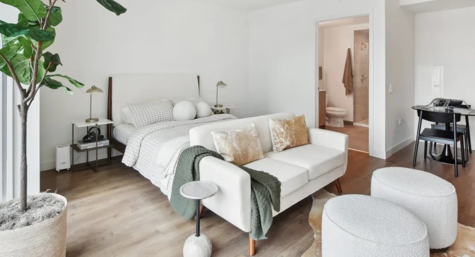 Spacious studio apartment layout featuring a comfortable bed, a small sofa, and an ensuite bathroom entrance at Cassidy on Canal in Chicago