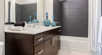 Modern bathroom at Catalyst apartments in Chicago with a dark wood vanity, white countertop, and tiled shower