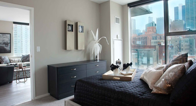 Cozy bedroom at Catalyst apartments in Chicago with a large window offering a city view, a dark bed, and modern decor