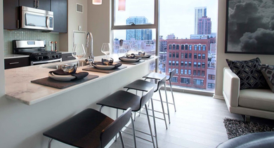 Open-concept kitchen and living area at Catalyst apartments in Chicago, with a kitchen island, bar stools, and large windows