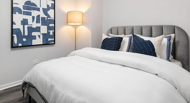 Cozy bedroom with a queen-sized bed, soft grey headboard, and blue accent pillows at Century Tower Apartments Chicago