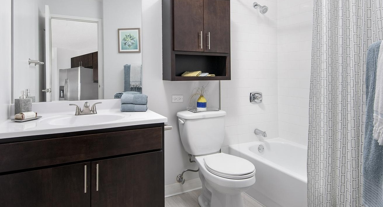 Contemporary bathroom at Chestnut Place apartments in Chicago featuring a dark wood vanity, white tiled shower, and mirror