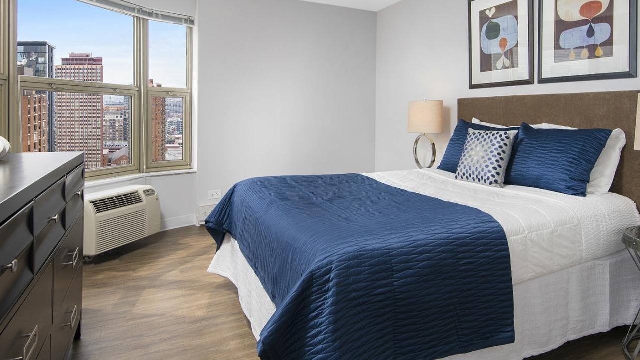 Modern bedroom at Chestnut Place apartments in Chicago with a large window offering city views and a comfortable bed