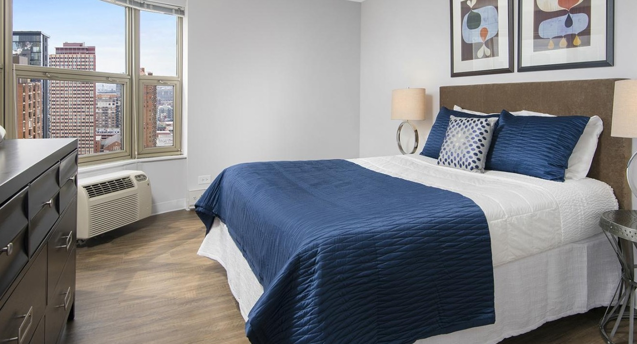 Modern bedroom at Chestnut Place apartments in Chicago with a large window offering city views and a comfortable bed