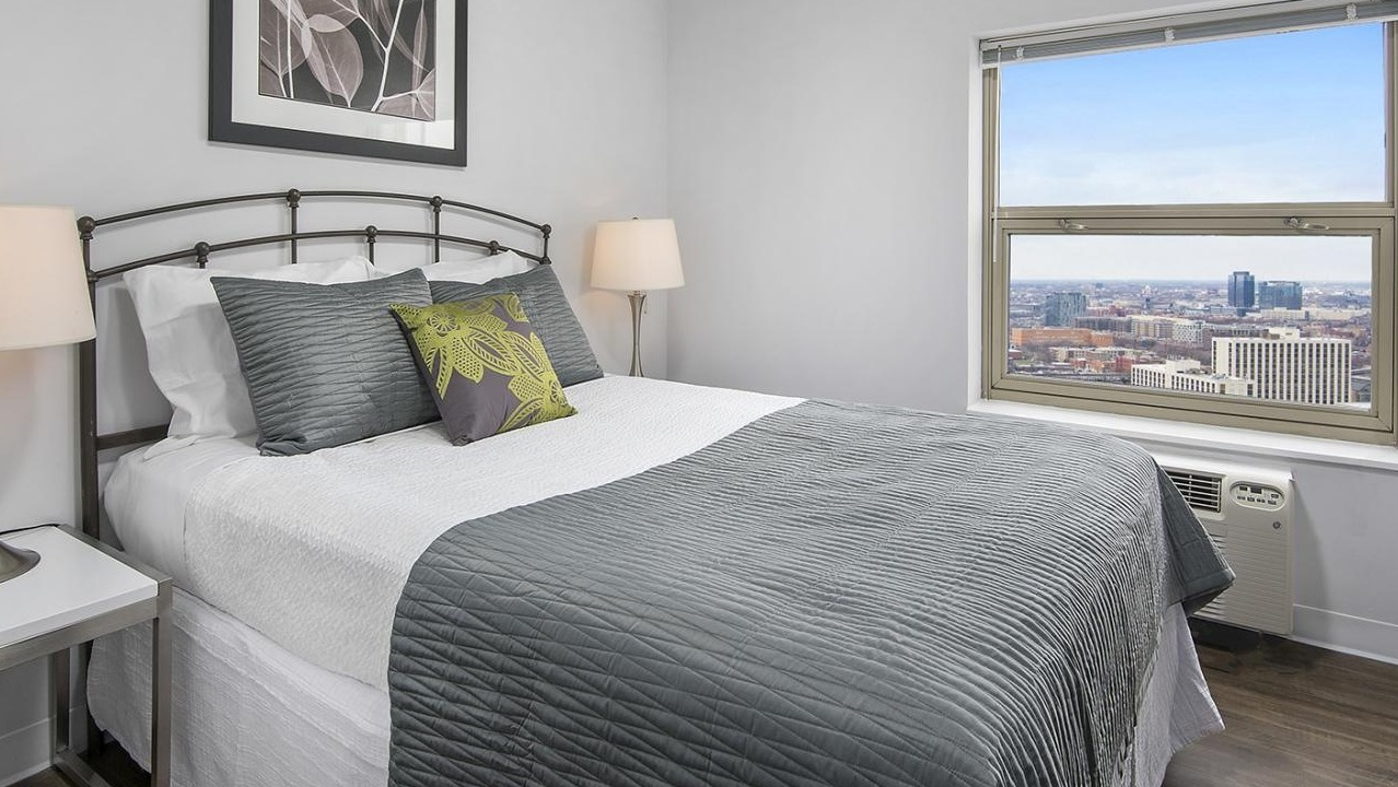 Charming bedroom at Chestnut Place apartments in Chicago with a large window overlooking urban views and hardwood floors