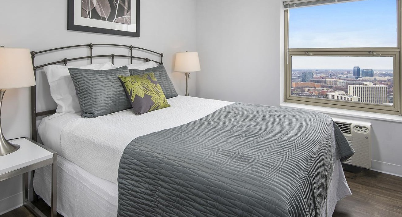 Charming bedroom at Chestnut Place apartments in Chicago with a large window overlooking urban views and hardwood floors