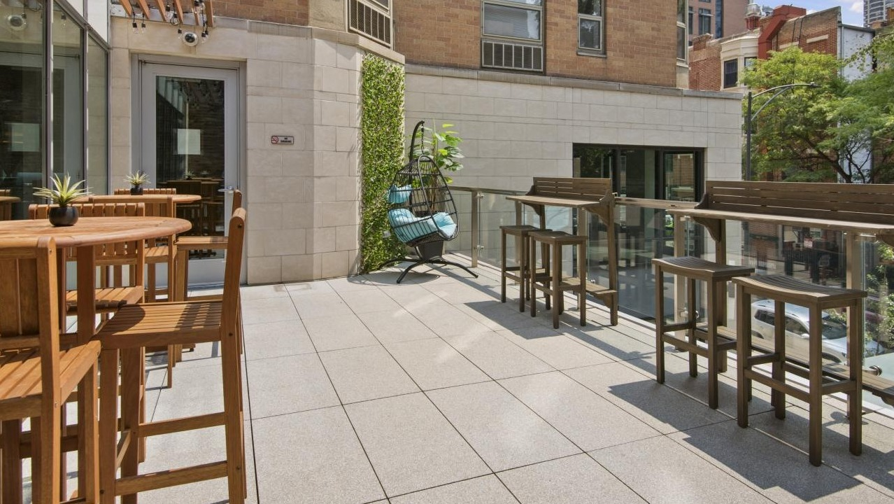 Charming outdoor patio at Chestnut Place apartments in Chicago with wooden tables, chairs, and lush greenery