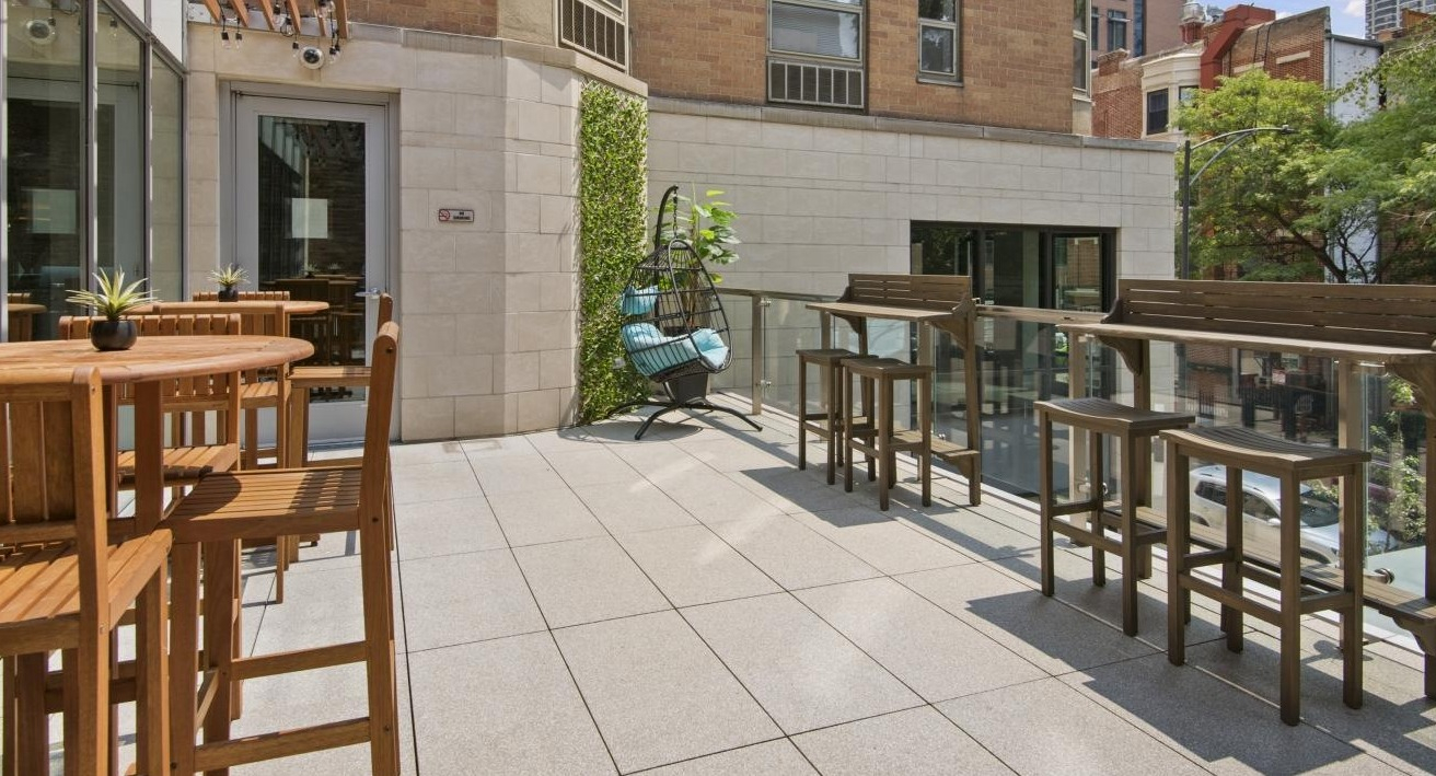 Charming outdoor patio at Chestnut Place apartments in Chicago with wooden tables, chairs, and lush greenery