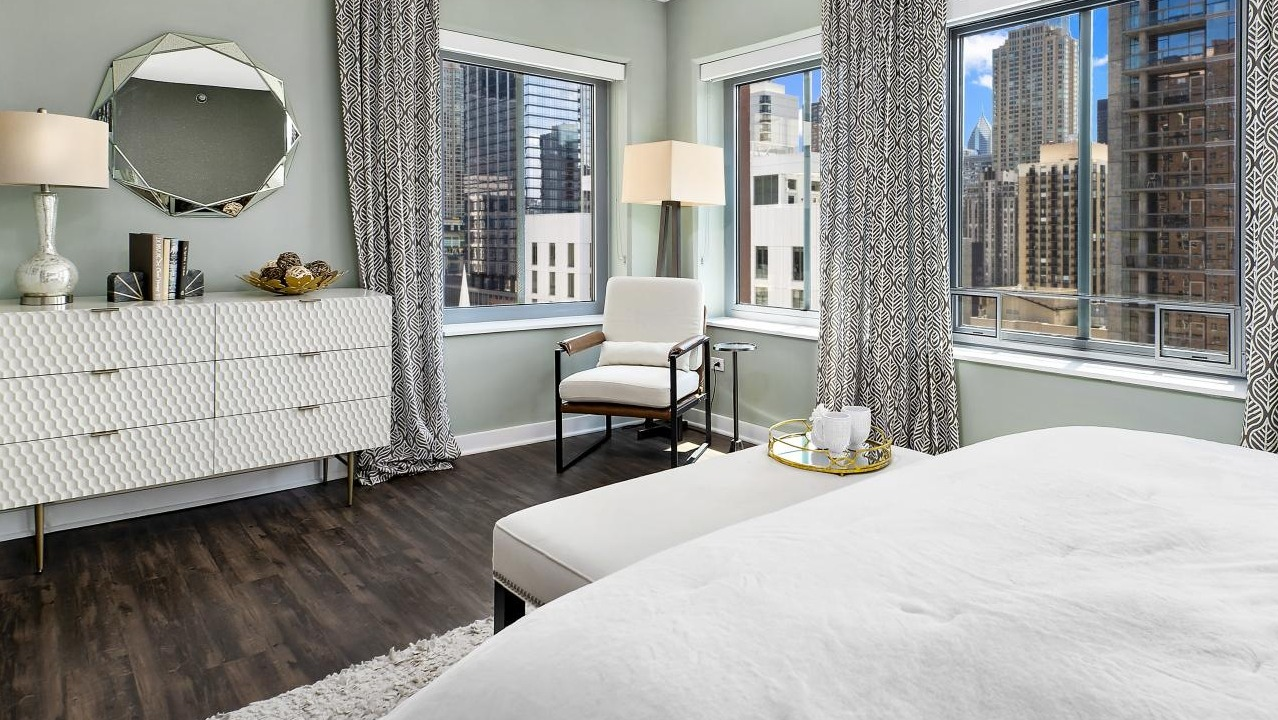 A stylish bedroom at Chestnut Towers, featuring a chic white dresser, a comfortable bed, and city views
