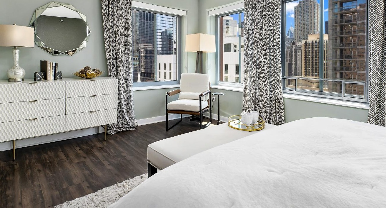 A stylish bedroom at Chestnut Towers, featuring a chic white dresser, a comfortable bed, and city views