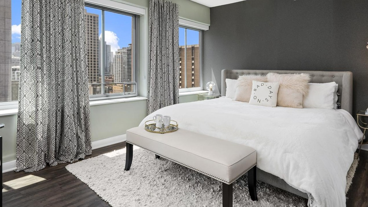 A cozy bedroom at Chestnut Towers, featuring a large bed with plush pillows, a soft rug, and city skyline views