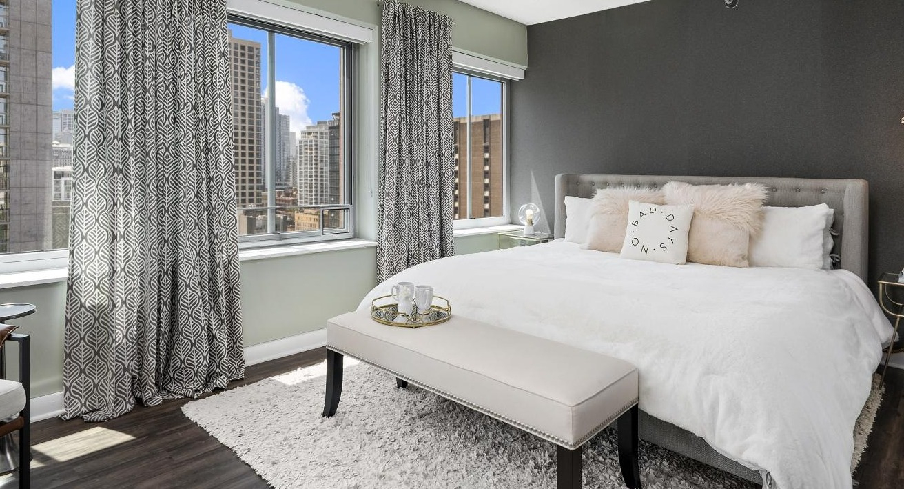 A cozy bedroom at Chestnut Towers, featuring a large bed with plush pillows, a soft rug, and city skyline views