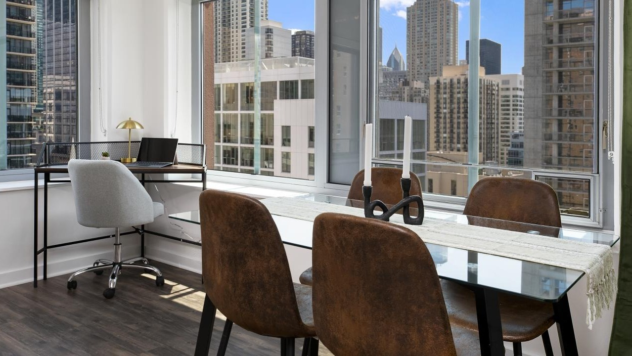 A modern dining area at Chestnut Towers, featuring a glass table, leather chairs, and bright windows with city views