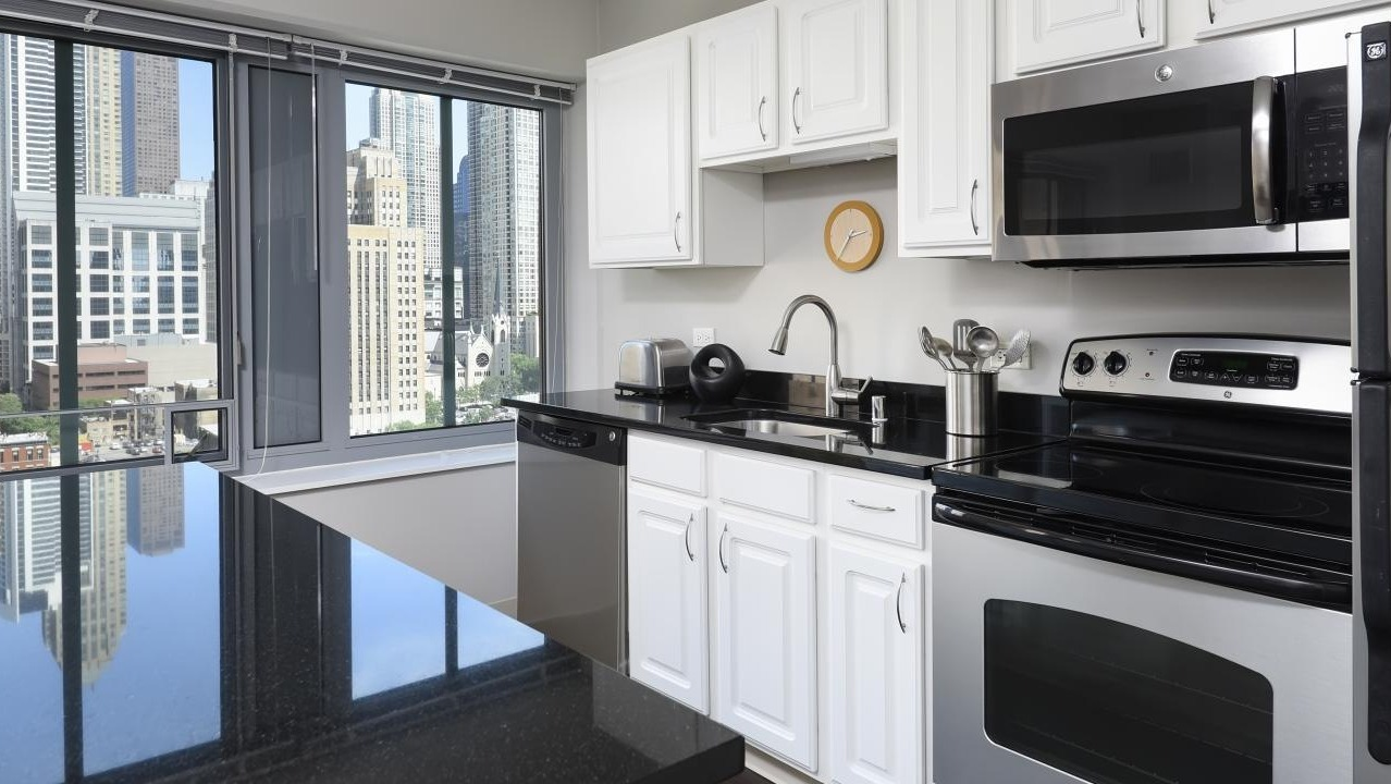 A modern kitchen at Chestnut Towers, equipped with white cabinetry, black countertops, and stainless steel appliances