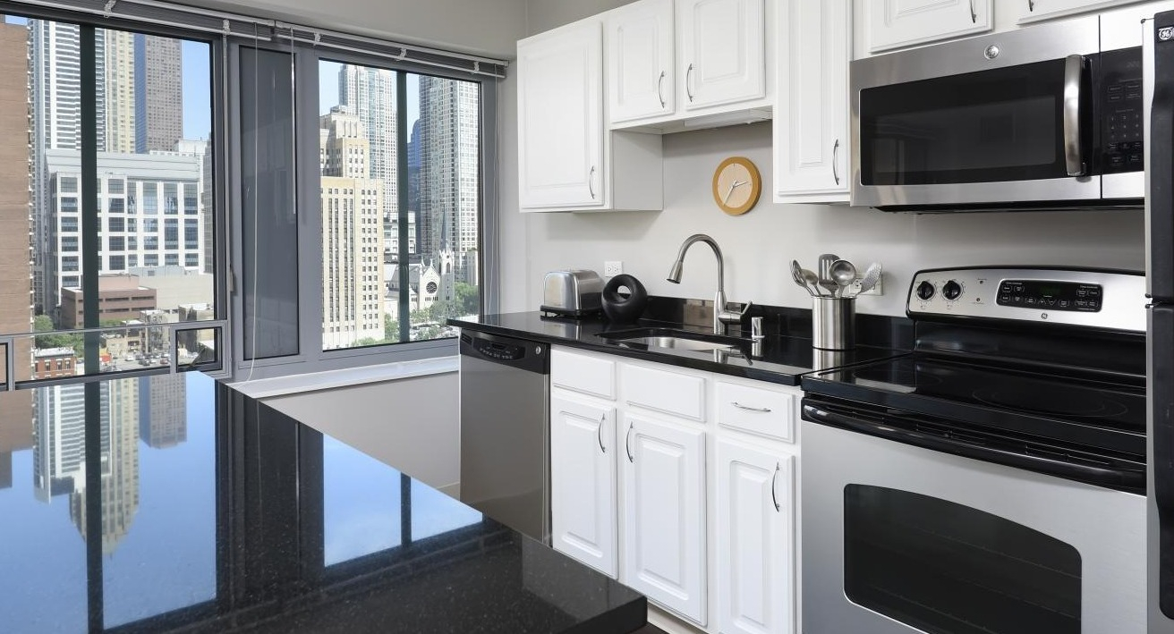 A modern kitchen at Chestnut Towers, equipped with white cabinetry, black countertops, and stainless steel appliances